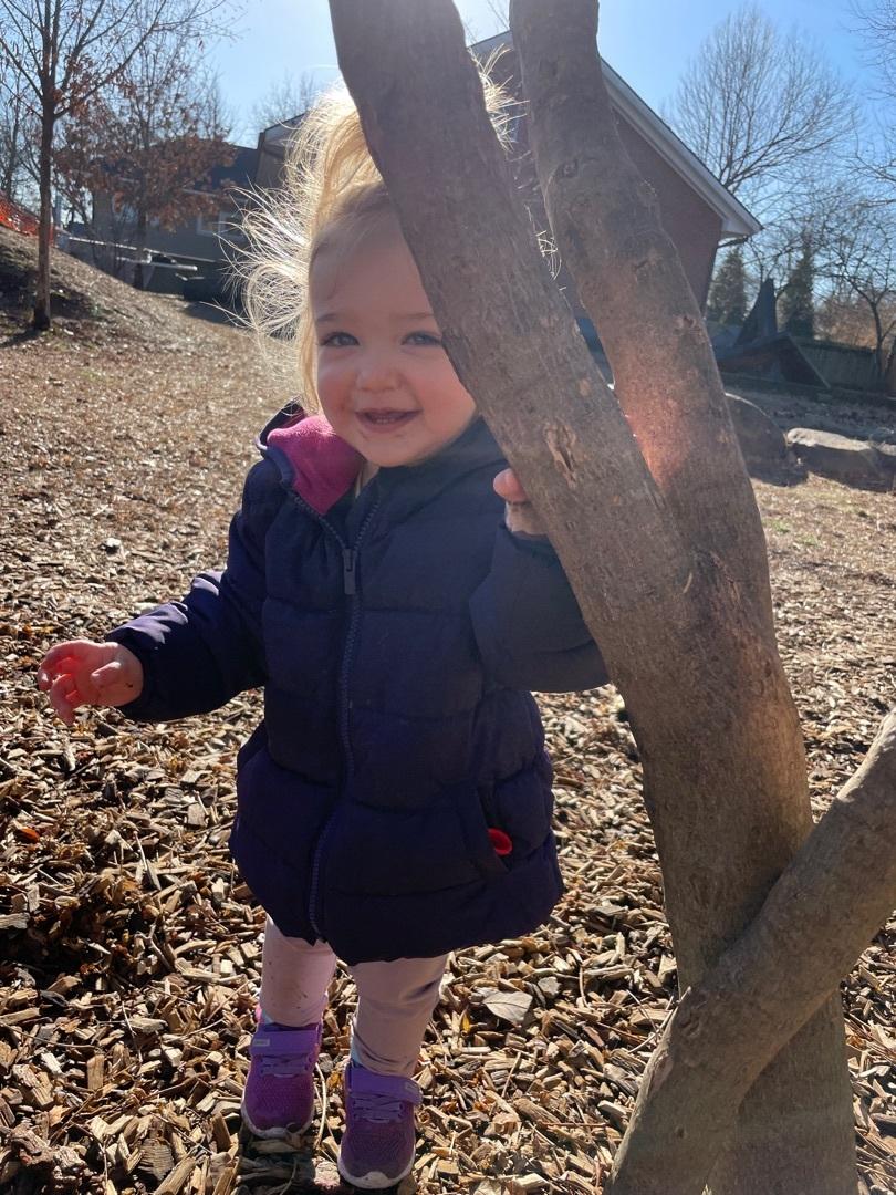 Child smiling behind a tree