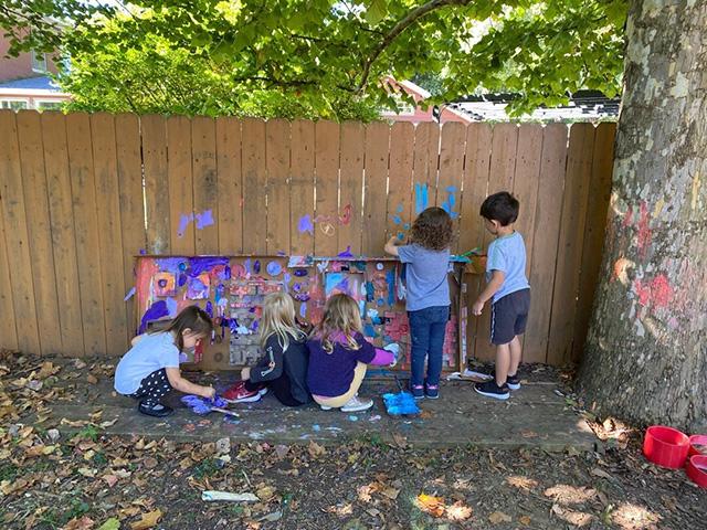 Several children painting on a wooden fence